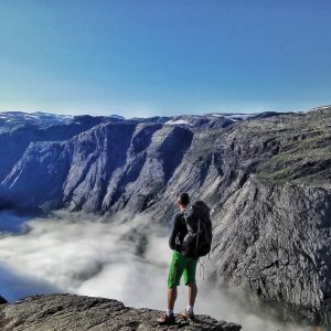 Турист с рюкзаком над окутанным облаками озером Рингедалсватнет на маршруте к Языку Тролля